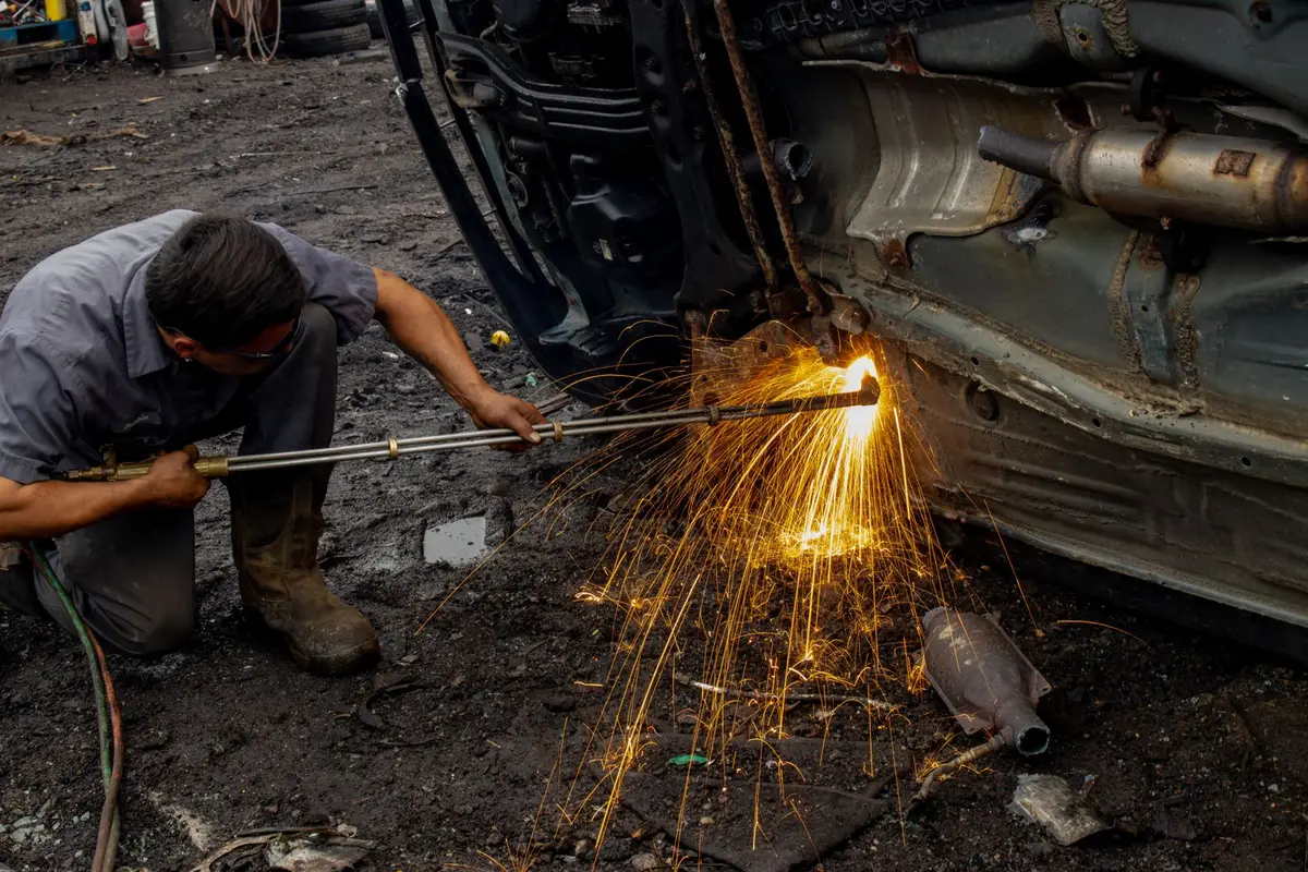 Welder kneeling beside a vehicle, sending sparks while working on the undercarriage frame outdoors